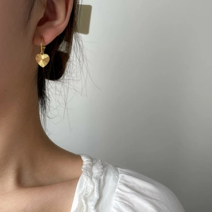 Close-up of elegant gold heart earrings with textured finish worn by a model