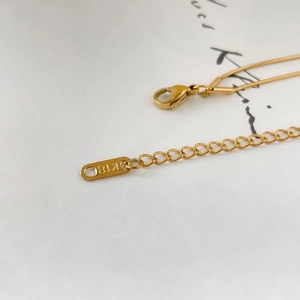 Macro detail of gold snake chain necklace featuring lobster clasp and K18 engraving tag