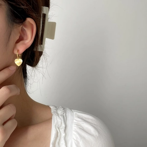 Close-up of elegant gold heart-shaped earrings with textured pattern worn by a model