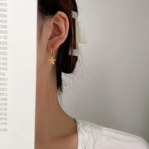 Detailed close-up of a gold star drop earring with textured radial patterns on a model