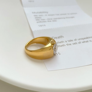 Detailed view of wide gold plated ring with large round zircon on white ceramic plate