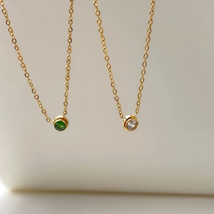 Dettaglio di collane girocollo in oro con pendenti tondi in zircone verde e bianco