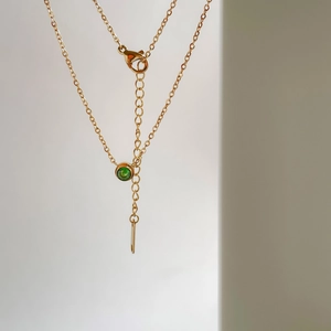 Dettaglio macro della collana dorata con pendente smeraldo rotondo e chiusura a moschettone