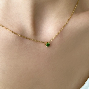 Collana girocollo dorata con ciondolo tondo in gemma verde sulla clavicola di una donna