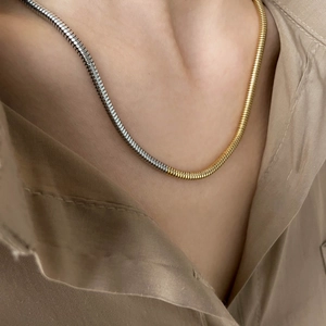 Détail d'un collier chaîne serpent bicolore or et argent sur un cou, finition brillante