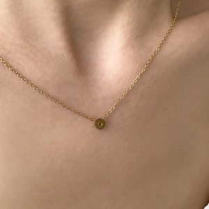 Dettaglio della collana d'oro minimalista con piccolo ciondolo a cerchio verde sul collo