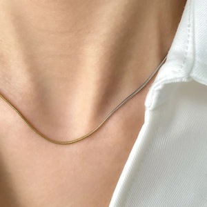 Gros plan d'un collier chaîne serpent bicolore or et argent sur le cou d'un modèle