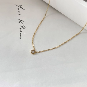 Dettaglio di una collana dorata con ciondolo tondo in zircone verde su carta bianca