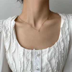 Dettaglio di una collana d'oro minimalista con ciondolo solitario rotondo su una modella