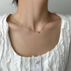 Dettaglio di una collana minimalista in oro con gemma verde rotonda indossata da una modella