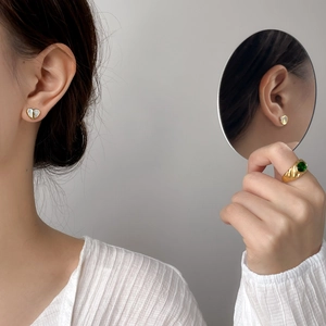 Dettaglio di orecchini a cuore in conchiglia e anello smeraldo con riflesso specchio