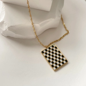 Close-up of golden rope chain with black and white checkered rectangle pendant on stone