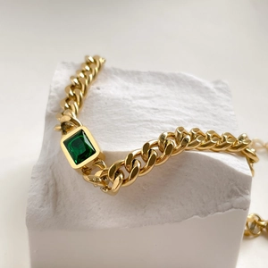 Detailed shot of emerald cut green gemstone on a chunky gold-plated chain bracelet