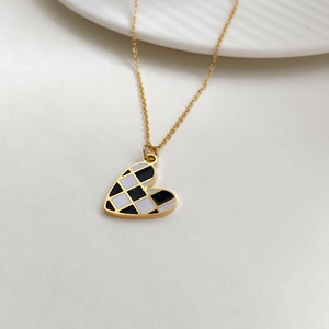 Close-up of golden necklace with black and white checkered heart pendant on white tray