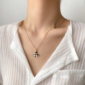 Close-up of model wearing black and white checkerboard heart necklace with gold chain