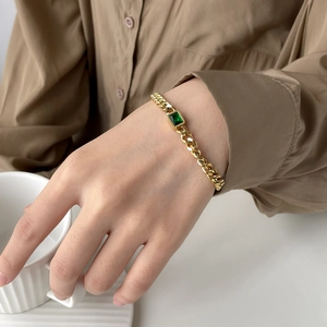 Close-up of a gold Cuban chain bracelet with emerald green zircon on a model wrist