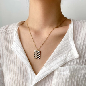 Detail of a gold necklace with a black and white checkerboard heart pendant on a model