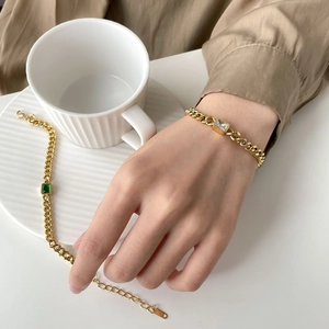 Macro detail of gold Cuban link bracelets with emerald and clear zircon stones