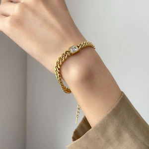 Detail view of a gold cuban chain bracelet with a square clear zircon stone on wrist