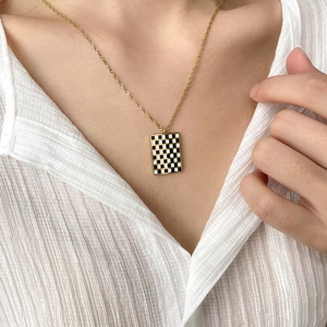 Close-up of golden checkered enamel pendant necklace worn on a white textured shirt