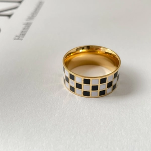 Detail shot of a wide gold-tone ring featuring a black and white checkerboard enamel pattern