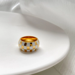Macro detail of wide checkered ring with gold and white enamel pattern on white dish