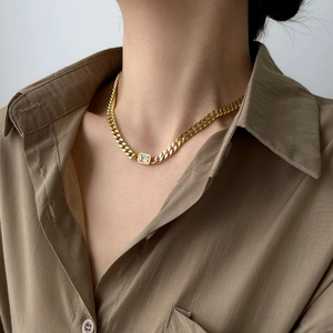 Close-up of golden Cuban link necklace with emerald-cut white zircon in natural lighting