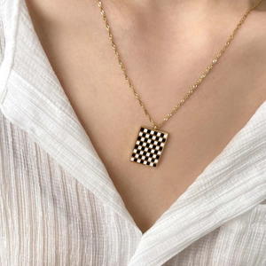Detail of a gold twisted chain necklace featuring a black and white checkered pendant