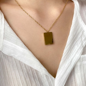 Close-up of golden rectangular polished pendant necklace worn on neck with white top