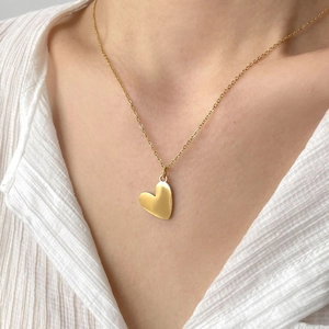 Close-up of golden heart pendant necklace worn with a white striped shirt