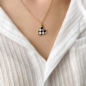 Close-up of heart-shaped checkerboard necklace worn over a white textured shirt