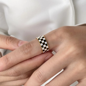 Close-up of a gold checkered ring with black and white enamel on a model's hand