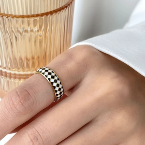 Detail of checkered enamel ring with golden band worn on hand against glass background