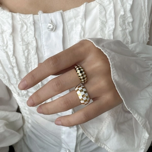 Close-up of checkerboard rings in black, gold, and white enamel on a hand