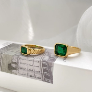 Detailed view of emerald-cut green gems and textured gold bands on a soft white background