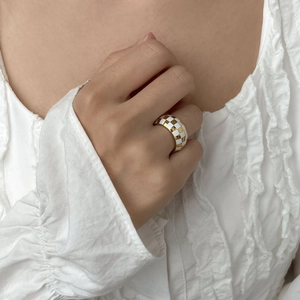 Macro detail of wide checkered ring in gold and white enamel on a model's finger