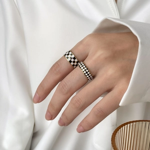 Detail of vintage gold checkerboard enamel rings worn on finger with silk background