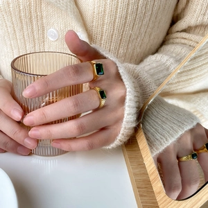 Close-up of golden rings with rectangular emerald stones on a beige knit sleeve