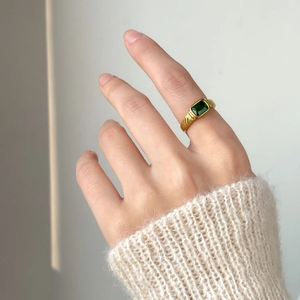 Close-up of square emerald cut green stone ring with textured gold band on hand