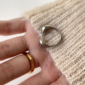 Macro detail of minimalist silver heart-shaped ring and wide gold band on a hand