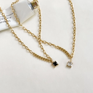 Elegant gold chain necklaces featuring black and clear square zircon pendants on white surface