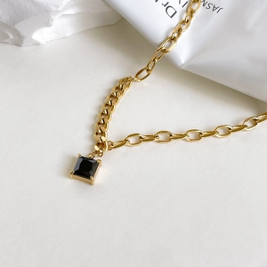 Macro shot of square black zircon pendant with golden chain and minimalist claw setting