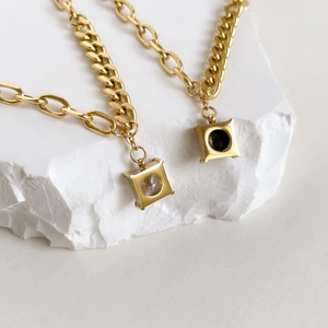 Detailed macro of gold square zircon pendant and black gemstone necklace on white stone