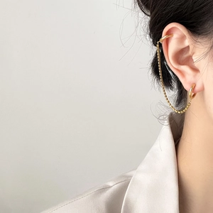 Detailed view of a gold chain cuff earring connecting a cartilage clip and lower hoop