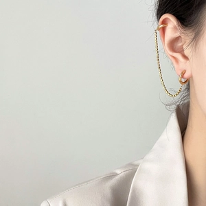 Detail of gold ear cuff and stud earring connected by a delicate square bead chain