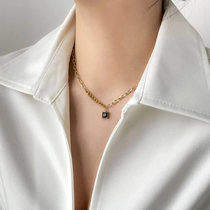 Detail of square black pendant on asymmetrical gold chain worn on white silk shirt