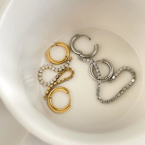 Detail of gold and silver hoop earrings with zircon pavé chains in a ceramic bowl