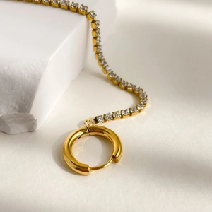 Detail of gold hoop earring with clear cubic zirconia tennis chain on white stone
