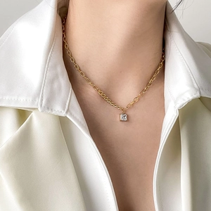 Detailed close-up of a square zircon pendant on a gold necklace worn by a model