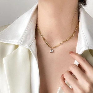Close-up of a gold square zircon pendant necklace on a model wearing white satin clothes